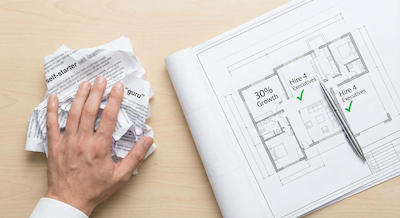A top-down desk shot. On the left side, there is a messy, crumpled pile of papers with blurred text and generic buzzwords like "self-starter" and "guru." A hand is pushing this pile away. On the right side, there is a clean, brightly lit architectural blueprint unfurled. The blueprint shows clear diagrams with specific metrics like "30% Growth" and "Hire 4 Executives," marked with green checkmarks. A sleek pen rests on the blueprint. The aesthetic is clean, professional, and focused.